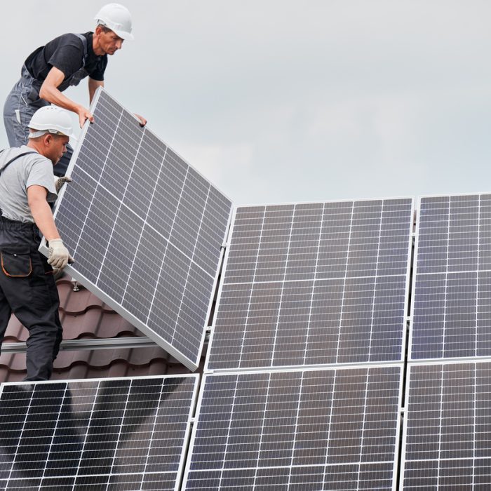 Men technicians mounting photovoltaic solar moduls on roof of house. Builders in helmets installing solar panel system outdoors. Concept of alternative and renewable energy.